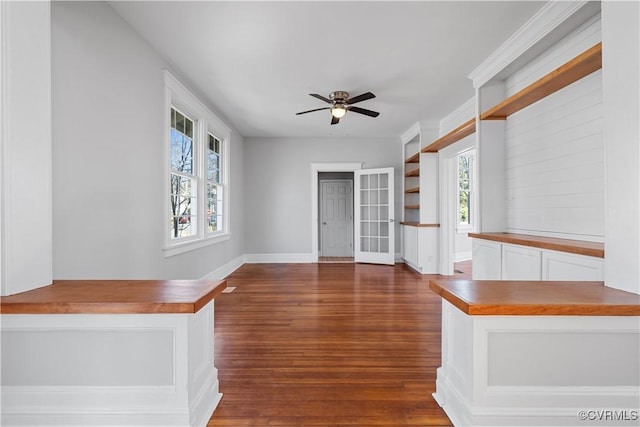 unfurnished living room featuring ceiling fan, dark wood finished floors, a wealth of natural light, and baseboards