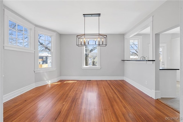 unfurnished dining area featuring hardwood / wood-style flooring, a notable chandelier, baseboards, and a wealth of natural light