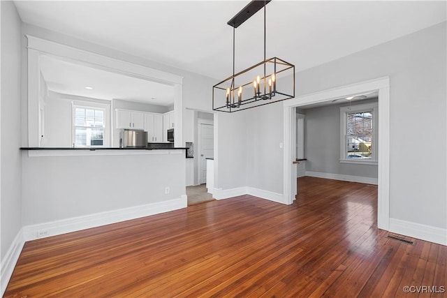 unfurnished dining area featuring hardwood / wood-style floors, an inviting chandelier, visible vents, and baseboards