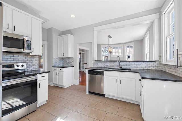 kitchen featuring tasteful backsplash, dark countertops, appliances with stainless steel finishes, white cabinetry, and a sink