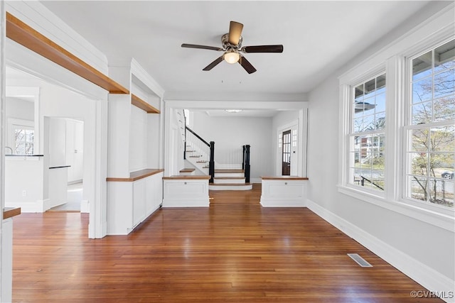 empty room featuring ceiling fan, dark wood-type flooring, visible vents, baseboards, and stairway