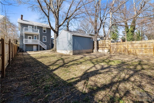 view of yard featuring a balcony, a fenced backyard, stairway, an outdoor structure, and a shed