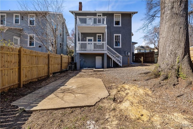 rear view of house featuring a chimney, a fenced backyard, a balcony, and stairs