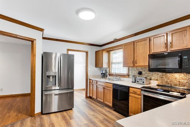 kitchen with black appliances, crown molding, light countertops, and a sink