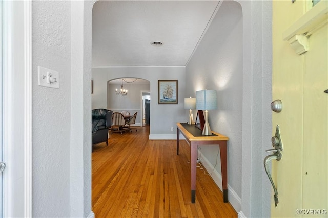 corridor featuring baseboards, visible vents, arched walkways, wood finished floors, and crown molding