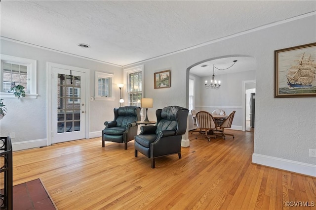 living area with light wood-style flooring, visible vents, arched walkways, and a textured ceiling