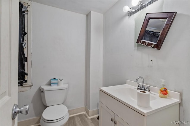 half bathroom with baseboards, vanity, toilet, and wood finished floors