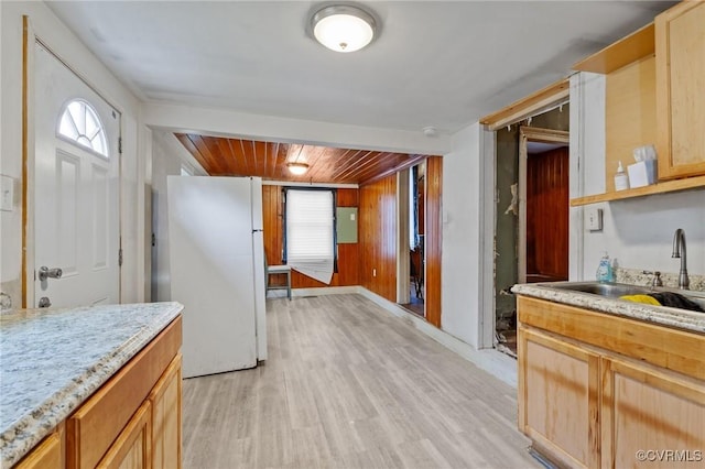 kitchen featuring light wood-style flooring, freestanding refrigerator, light brown cabinets, a sink, and wooden walls