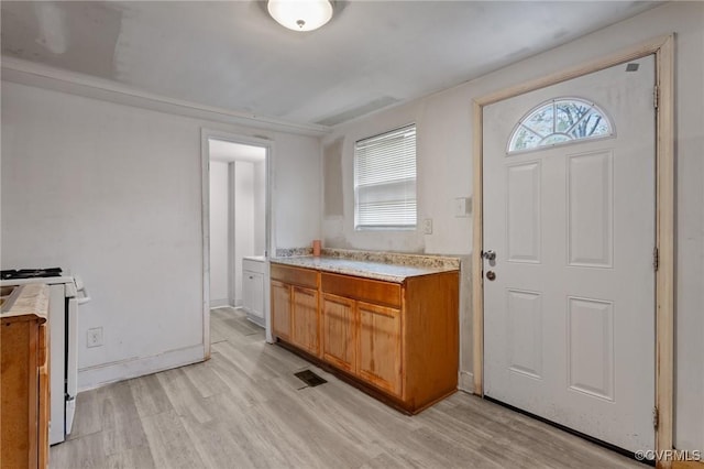 kitchen with brown cabinets, light wood-style floors, white range oven, and light countertops