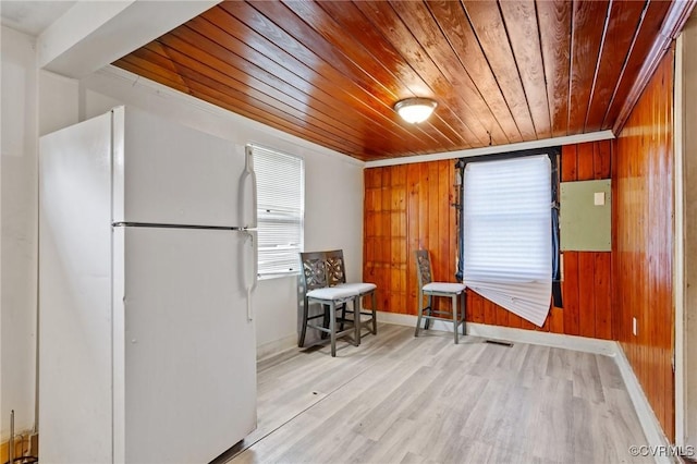 interior space with wood ceiling, light wood-type flooring, freestanding refrigerator, and wooden walls