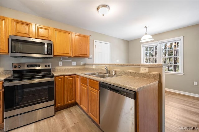 kitchen with a sink, light countertops, appliances with stainless steel finishes, light wood finished floors, and pendant lighting