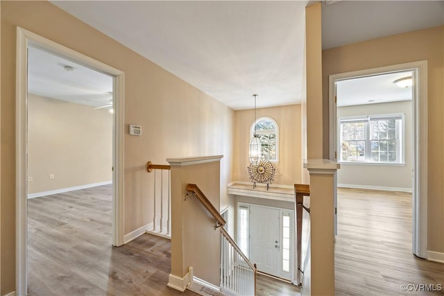 corridor with a healthy amount of sunlight, baseboards, wood finished floors, and an upstairs landing