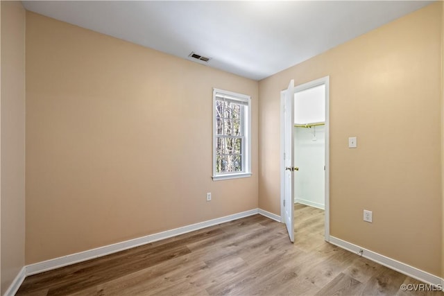 unfurnished bedroom with light wood-type flooring, baseboards, visible vents, and a walk in closet