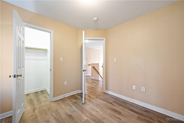 unfurnished bedroom with light wood-style flooring, baseboards, a walk in closet, and a closet