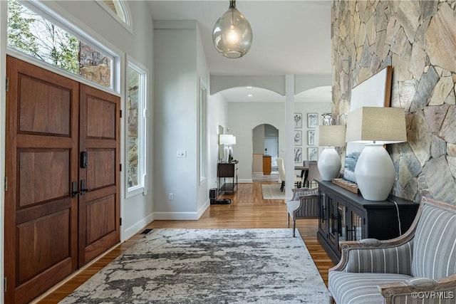 entrance foyer with baseboards, arched walkways, wood finished floors, and a healthy amount of sunlight