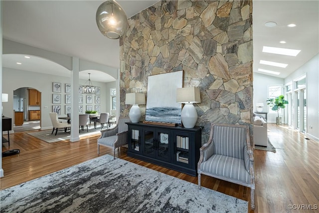 living room featuring arched walkways, wood finished floors, an inviting chandelier, and vaulted ceiling with skylight