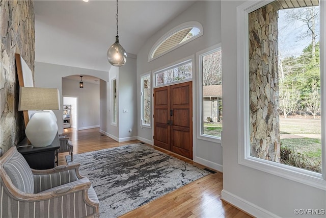 entryway featuring arched walkways, wood finished floors, baseboards, and vaulted ceiling