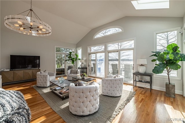 living room featuring high vaulted ceiling, a skylight, wood finished floors, a notable chandelier, and baseboards