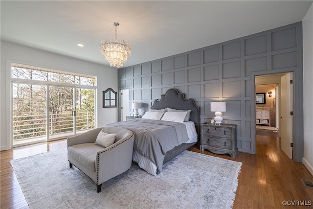 bedroom featuring a chandelier, a decorative wall, wood finished floors, and visible vents