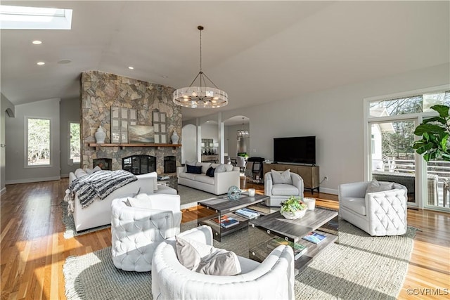 living area featuring vaulted ceiling with skylight, arched walkways, a chandelier, and a healthy amount of sunlight