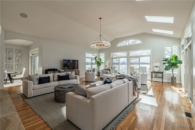 living room with arched walkways, vaulted ceiling with skylight, visible vents, and wood finished floors