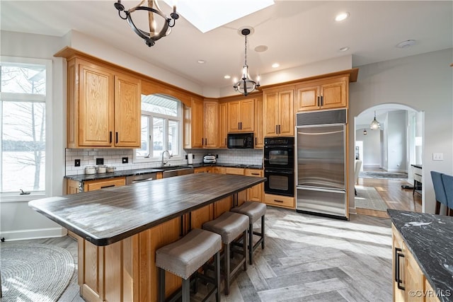 kitchen featuring an inviting chandelier, a kitchen breakfast bar, arched walkways, black appliances, and a sink