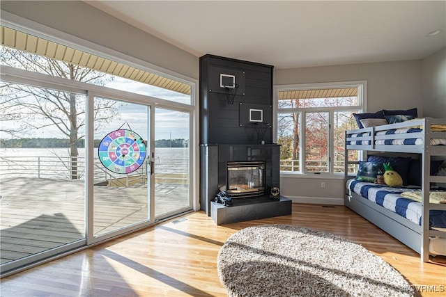 bedroom with baseboards, a water view, a fireplace, wood finished floors, and access to outside