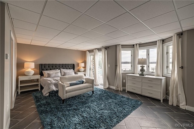bedroom featuring access to outside, multiple windows, a drop ceiling, and baseboards