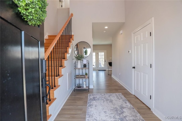 foyer with stairs, a high ceiling, baseboards, and wood finished floors