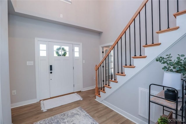 entryway with visible vents, stairway, a towering ceiling, wood finished floors, and baseboards