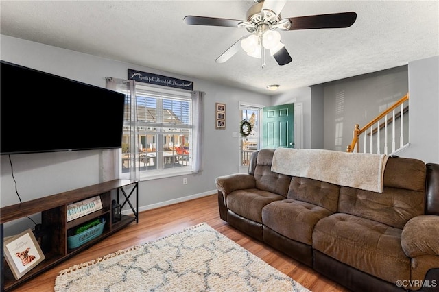 living area with baseboards, a ceiling fan, wood finished floors, stairs, and a textured ceiling