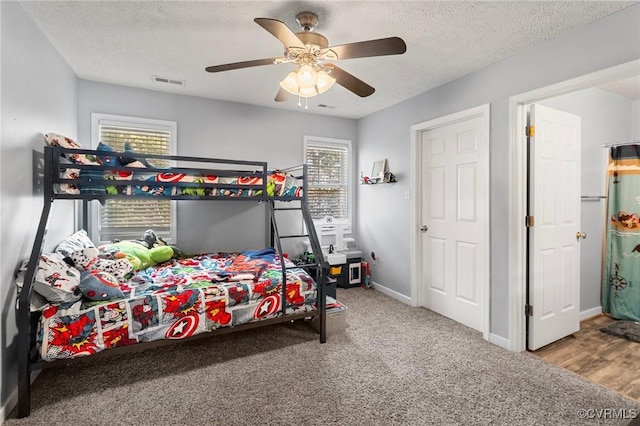 carpeted bedroom featuring a textured ceiling, ceiling fan, multiple windows, and baseboards