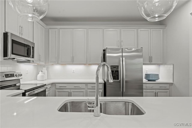 kitchen with appliances with stainless steel finishes, white cabinets, light countertops, and a sink