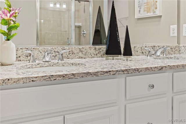 bathroom featuring double vanity, a stall shower, and a sink