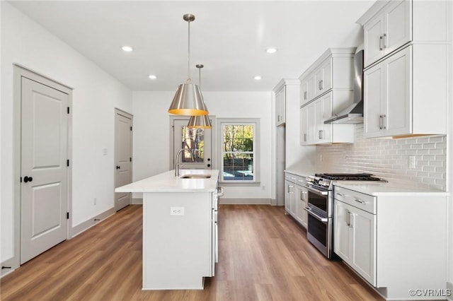 kitchen with range with two ovens, wall chimney range hood, light countertops, and decorative light fixtures