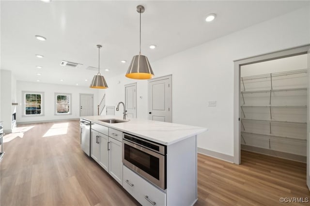 kitchen featuring decorative light fixtures, open floor plan, white cabinets, a sink, and light stone countertops