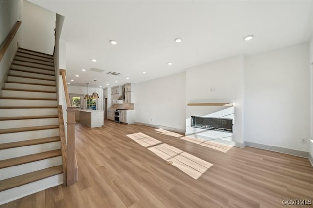 unfurnished living room featuring light wood-type flooring, a fireplace with flush hearth, stairway, and recessed lighting