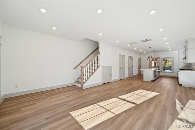 unfurnished living room featuring light wood finished floors, stairway, visible vents, and recessed lighting