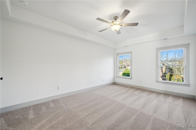 carpeted spare room featuring a tray ceiling, a ceiling fan, and baseboards