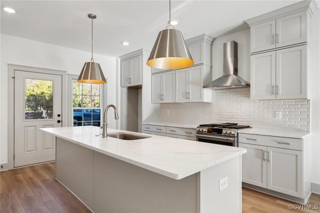 kitchen with wall chimney exhaust hood, decorative light fixtures, light stone countertops, stainless steel stove, and a sink