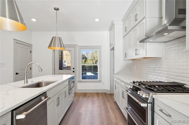 kitchen with stainless steel appliances, a sink, white cabinets, wall chimney range hood, and pendant lighting