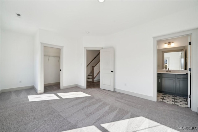 unfurnished bedroom with connected bathroom, light carpet, a sink, and baseboards