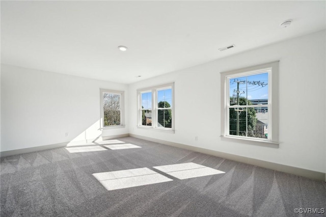 carpeted empty room featuring baseboards, visible vents, and a healthy amount of sunlight