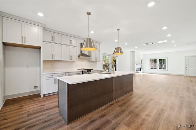 kitchen featuring pendant lighting, a center island with sink, light countertops, backsplash, and stainless steel gas range oven