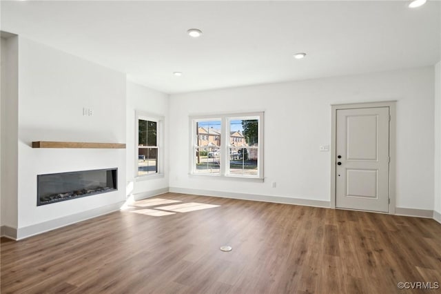 unfurnished living room with dark wood-type flooring, a glass covered fireplace, baseboards, and recessed lighting