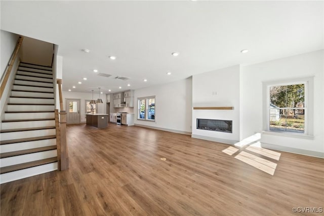 unfurnished living room featuring visible vents, wood finished floors, stairs, a fireplace, and recessed lighting