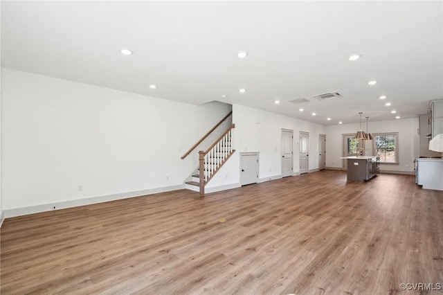 unfurnished living room with recessed lighting, visible vents, baseboards, light wood-style floors, and stairway