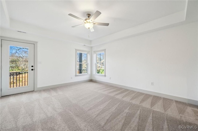 carpeted spare room with a tray ceiling, a ceiling fan, and baseboards