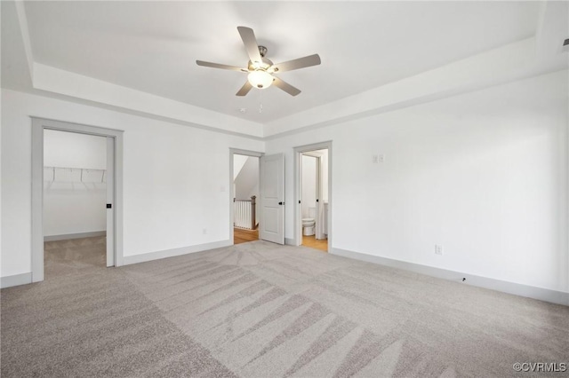 unfurnished bedroom featuring light carpet, a tray ceiling, and a walk in closet