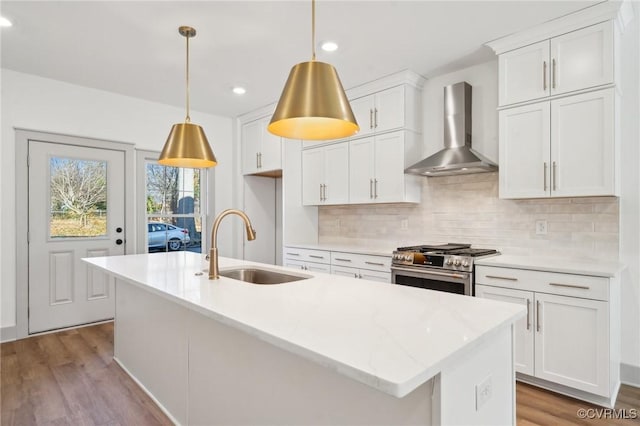 kitchen with hanging light fixtures, wall chimney range hood, stainless steel gas range, and white cabinetry